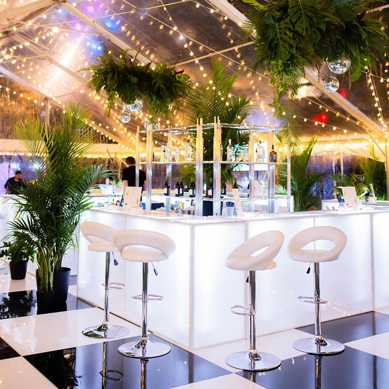 modern bar and bar stools on a black checkered floor with palm plants and cafe lighting for a Miami-themed corporate party
